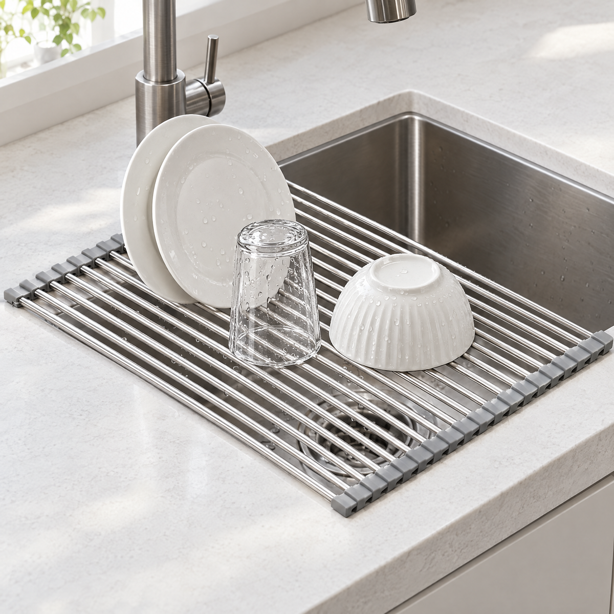 Roll-up dish drying rack laid across a kitchen sink holding two plates, a glass and a bowl
