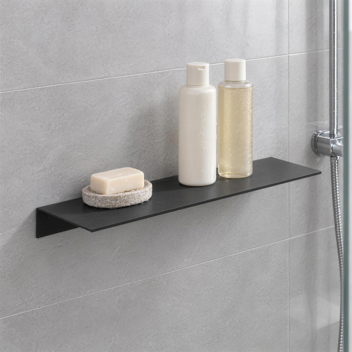 Matte black floating shelf on grey shower tile holding shampoo bottles and a bar of soap
