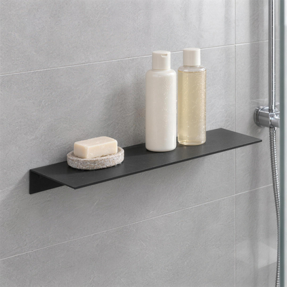 Matte black floating shelf on grey shower tile holding shampoo bottles and a bar of soap