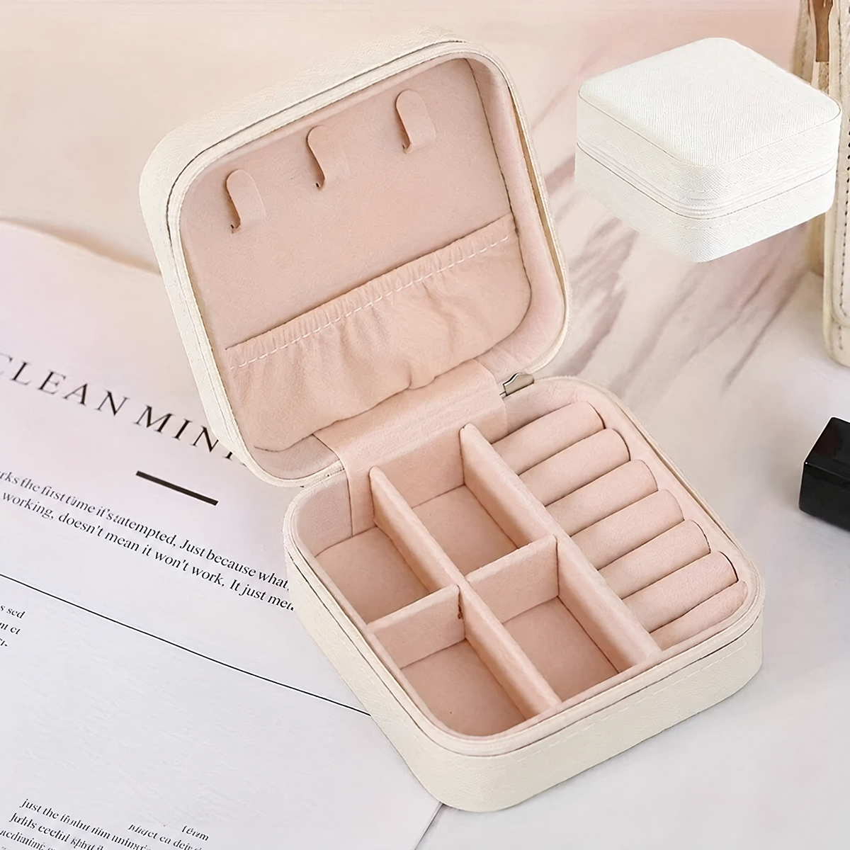 White travel jewelry case open and empty, showing the pink lining, lid hooks and compartments
